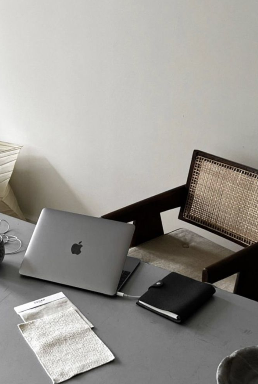 A quiet workspace with a laptop, notebook and cane chair on a grey desk