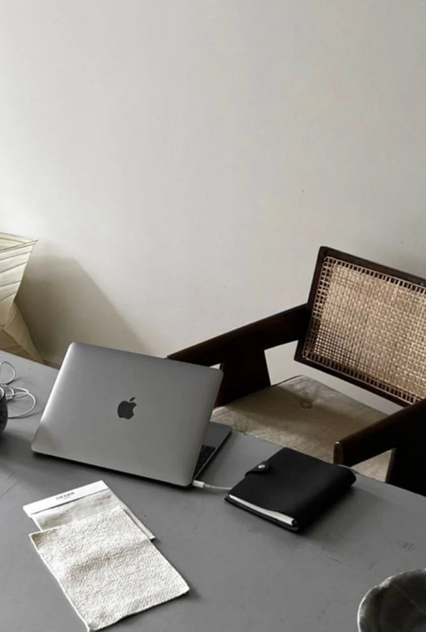 A quiet workspace with a laptop, notebook and cane chair on a grey desk